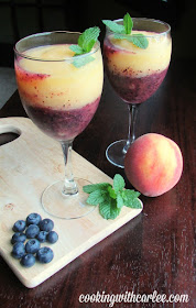 What a perfect way to cool off! These delicious peach and blueberry wine slushies are pretty, refreshing and only take a few ingredients and a couple of minutes to make! 2 wine glasses with layers of peach and blueberry wine slushy next to peaches, blueberries and fresh mint leaves