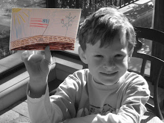 Boy holding card with American flag drawing.