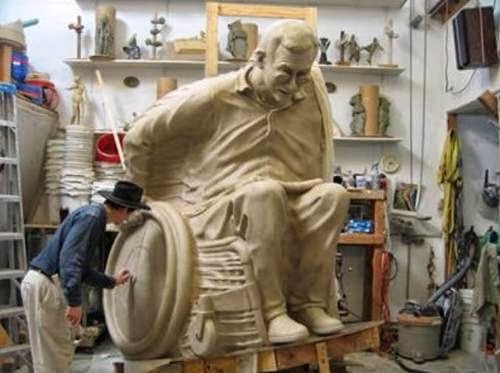Man working on a large-scale sculpture of a man in a wheelchair