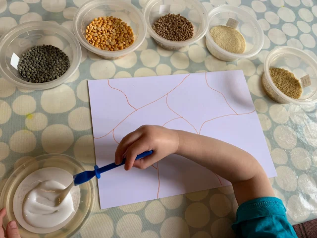 Set up showing bowls of grains and pulses, glue and card with a toddler ready to go
