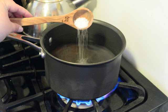 A pot of water, on a burner, with salt being added to it. 