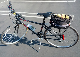 Whisk broom under cargo net atop bag mounted on rear bicycle rack.