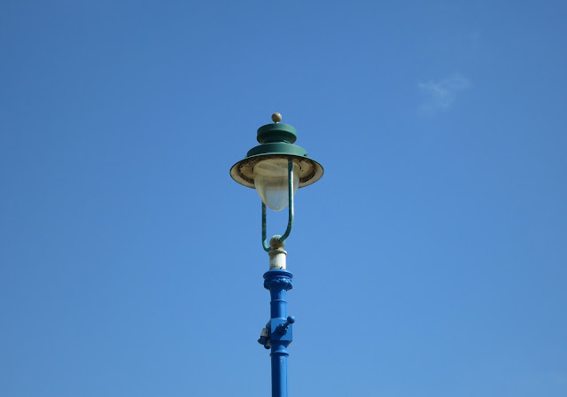 Blue and white lampost against almost cloudless blue sky.