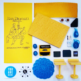 Flat lay of various items in yellow, black and white, mainly in one-twelfth scale miniature.