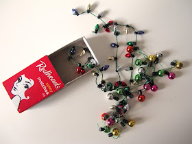 Matchbox with two strings of miniature Christmas lights spilling out of it.