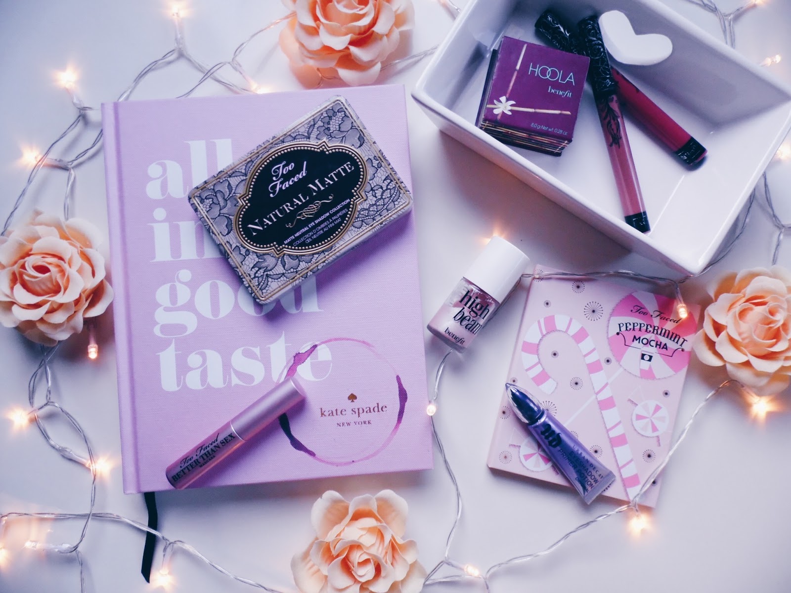 flat lay of book, palette, fairy lights, mascara, roses and more make up