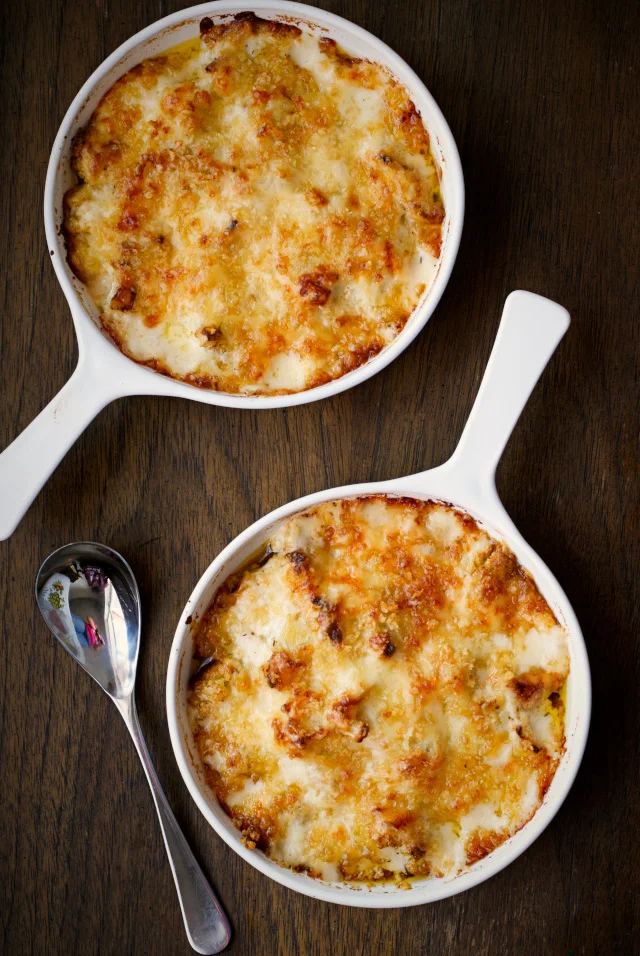 Roasted Cauliflower and Gruyère Gratin in two white vintage round casserole dishes on a wooden background.