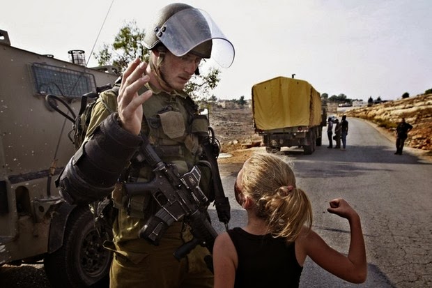 A Palestinian girl raises her fist against an Israeli soldier