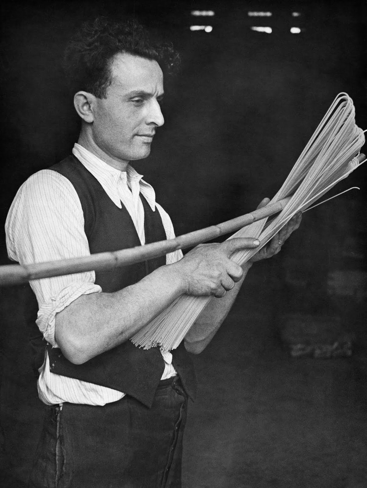 An Italian factory worker bends dried spaghetti with a stick. 1932.