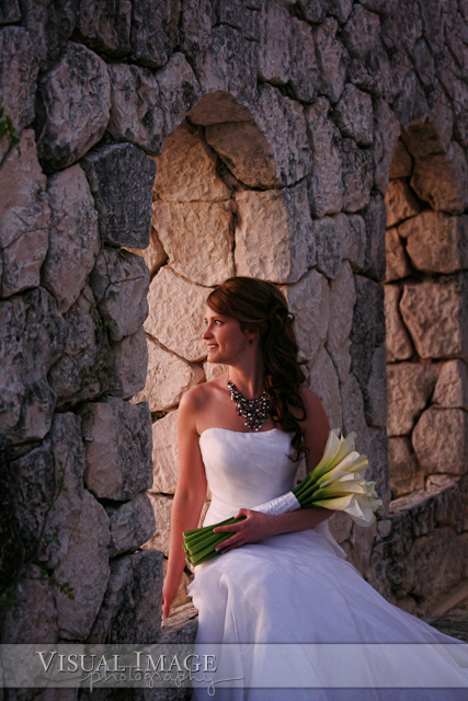 Portrait of bride sitting on stone wall with sunset coming through window