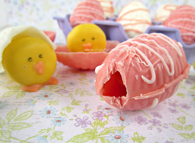 pink chocolate easter egg with crack and a baby chick mini oreo behind on flower surface