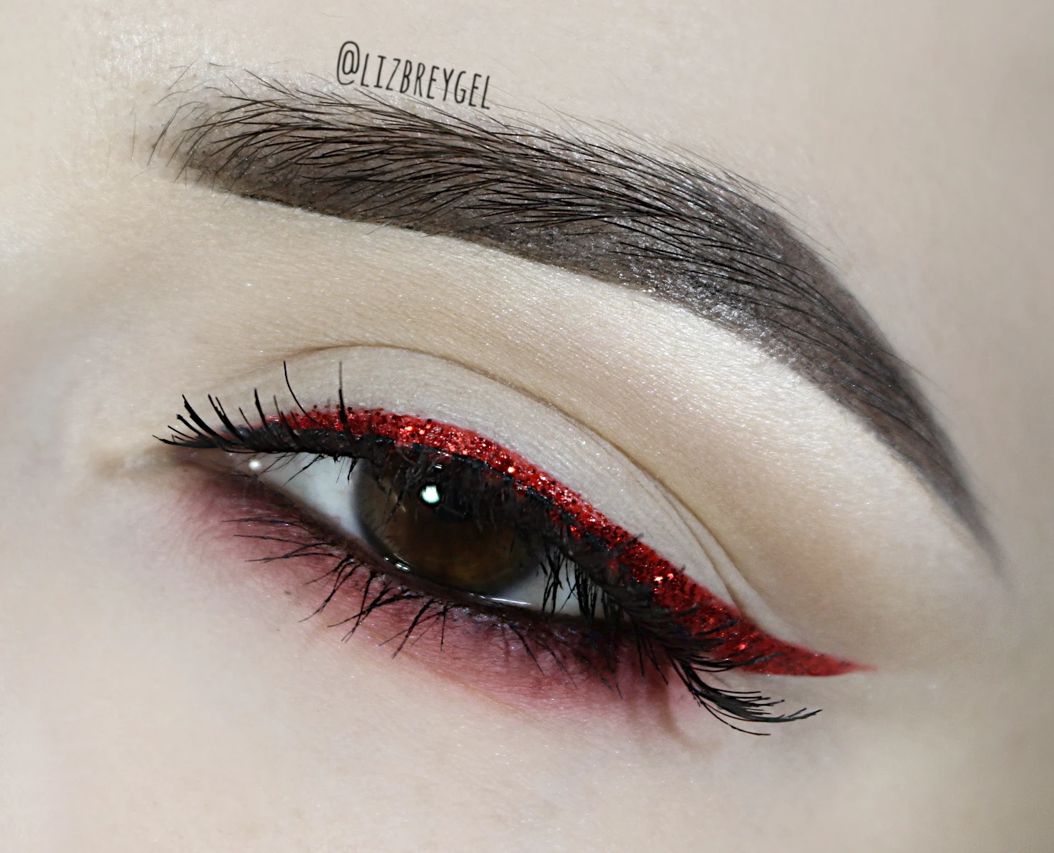 a close-up of a brown eye with a glamorous, red glitter eye look for Christmas