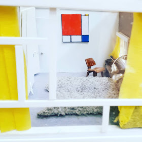 View through the window of a 1/48-scale mid-century modern house, showing a bedroom in white with accents of bright colour.