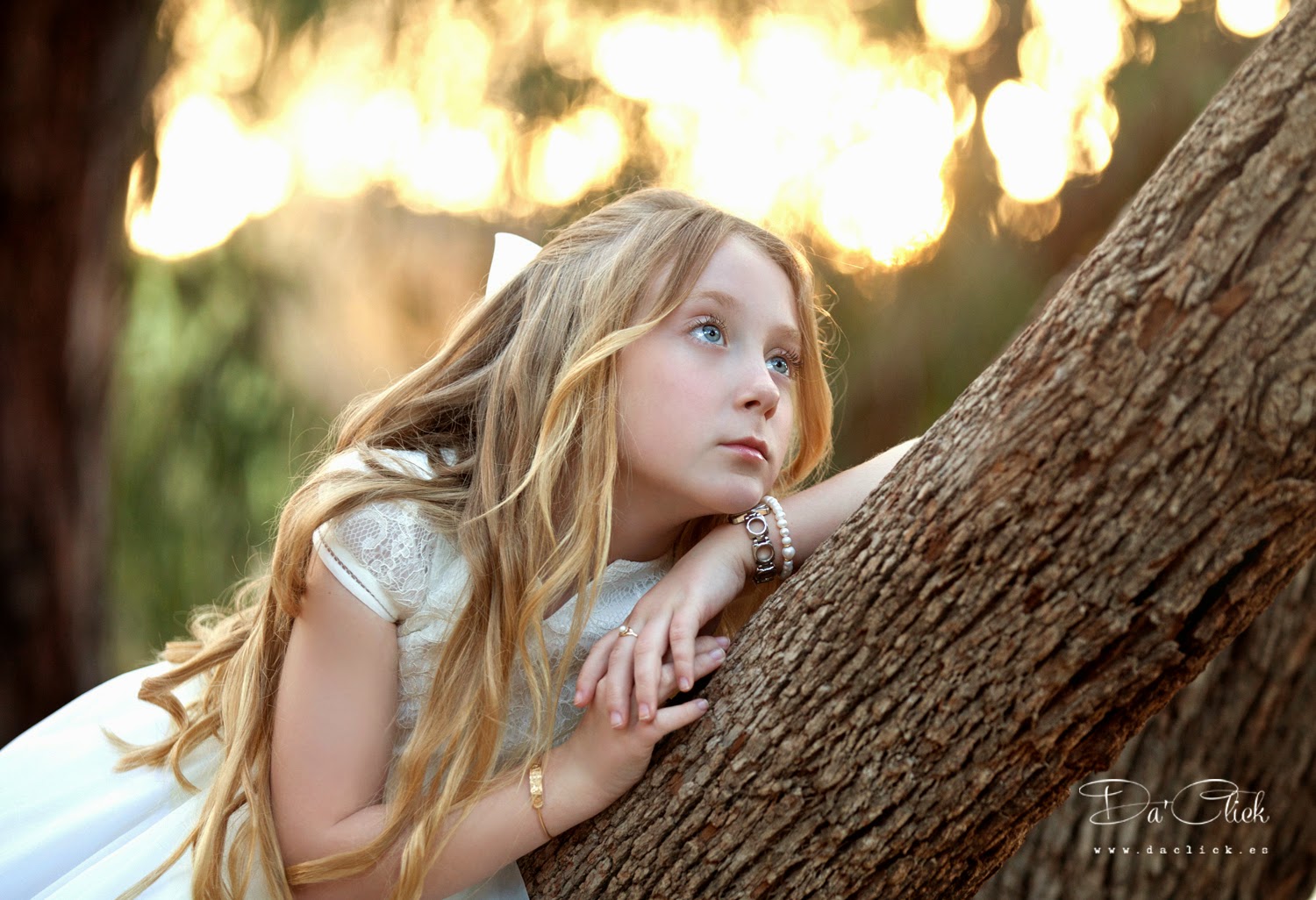 Retrato de niña de comunión en exterior, apoyada en arbol mirando al horizonte