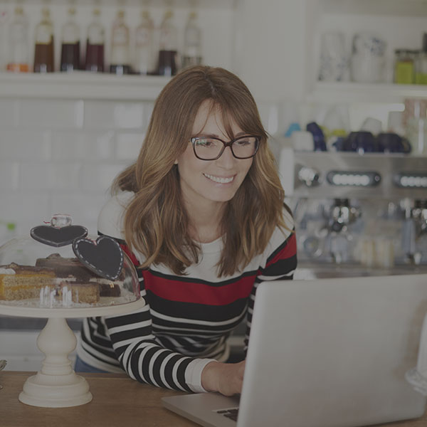Close-up shot of a smiling cafe owner standing at counter and using laptop