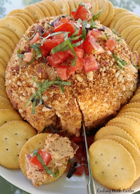 Bacon and bruschetta get all cozy together is a fun cheese ball that is a perfect summer appetizer. knife cutting into bacon bruschetta cheese ball with some spread on a cracker