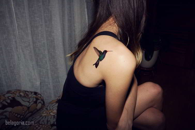 Mujer sentada con tatuaje de un colibrí en el omóplato.