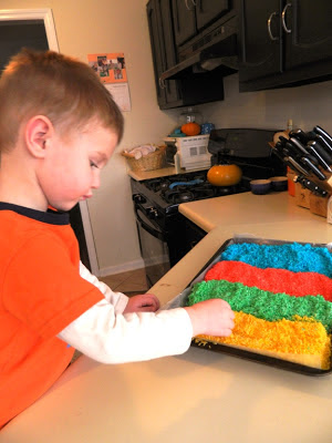 Young boy at kitchen counter with four rows of colored rice on a blue tray