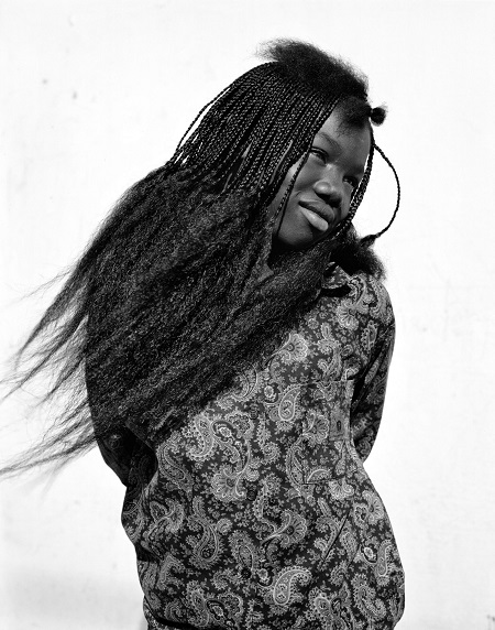 Retrato de una joven afroamericana con cabello largo y trenzado y vestido patronado. Foto en blanco y negro.