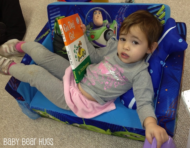 toddler laying on a small couch reading a Dr. Suess book