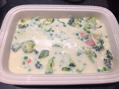 white sauce poured over salmon and veg in a casserole dish
