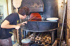 Chef placing a vegetarian pizza in wood-burning oven, Ukauka