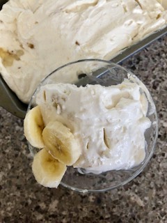 A crystal dish of banana ice cream viewing from the top, with the pan of the banana ice cream behind it