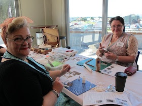 Two women dressed in 1940s outfits, crafting on a table at a workshop.