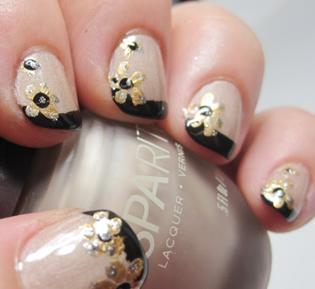 Gold flowers over a black French tip and nude nail with topcoat