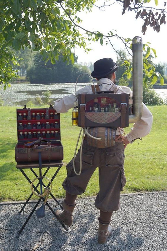 Man dressed as steampunk bartender with mobile bar in his backpack and suitcase, full of liquor and alcohol bottles and glasses. Men's steampunk costumes