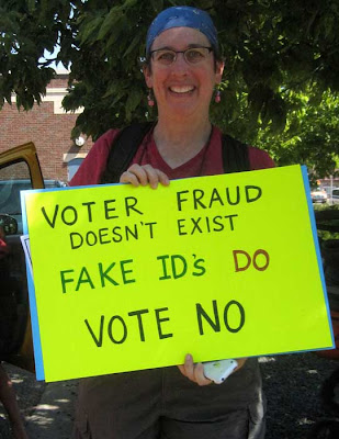 Woman holding hand-lettered sign reading Voter Fraud Doesn't Exist, Fake IDs Do