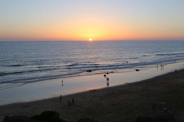 Una playa, el mar y el sol escondiéndose en el horizonte.