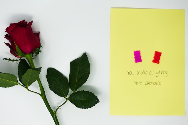 a red rose and a yellow card with two gel a peel bears on and message