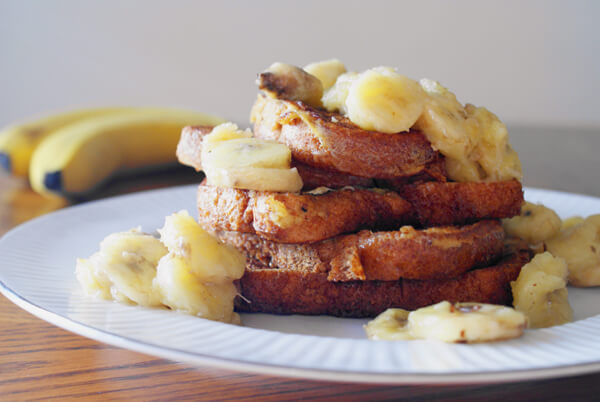 Five pieces of french toast on a white plate topped with caramelized bananas.