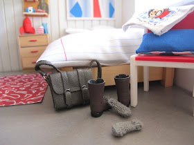 Modern one-twelfth scale miniature leather satchel, boots and socks dumped on the floor at the end of a bed.