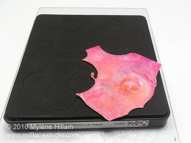 A piece of marbled pink resin placed over the circles of a circle die.