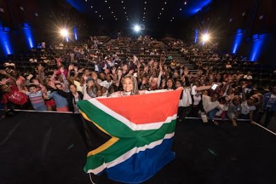 Raven Symone at Disney Raven's Home Premiere Raven Symone holding South African flag with theatre full of fans in background