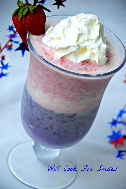 two red white and blue milkshake with whipped cream and a strawberry on top as garnish 