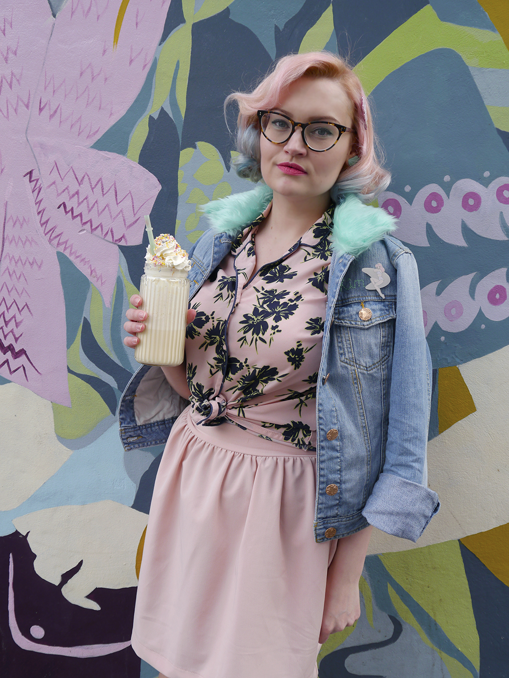 Scottish fashion blogger Kimberley from Wardrobe Converations with candy coloured hair and DIY retro denim jacket standing against grafitti background with milkshake