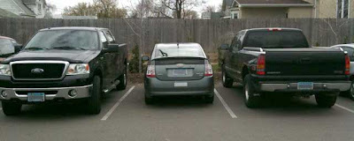Gray Prius parked between two black full-sized pickup trucks