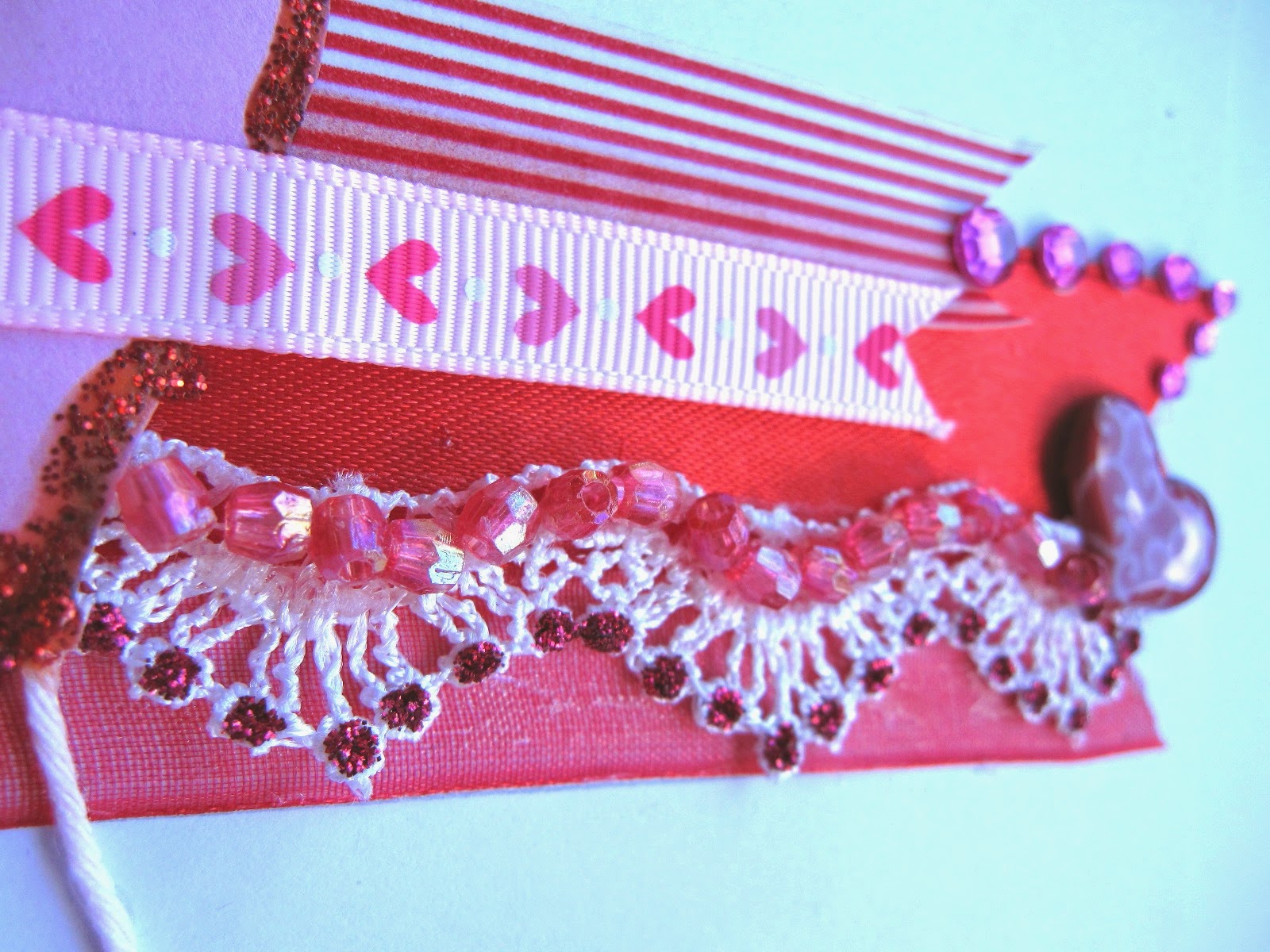 detalle tarjeta scrapbooking San Valentín con superposición en rojo y rosa de cintas, washi tape, encaje, corazón brad con glossy accents, diamantes autoadhesivos y cuentas 3D