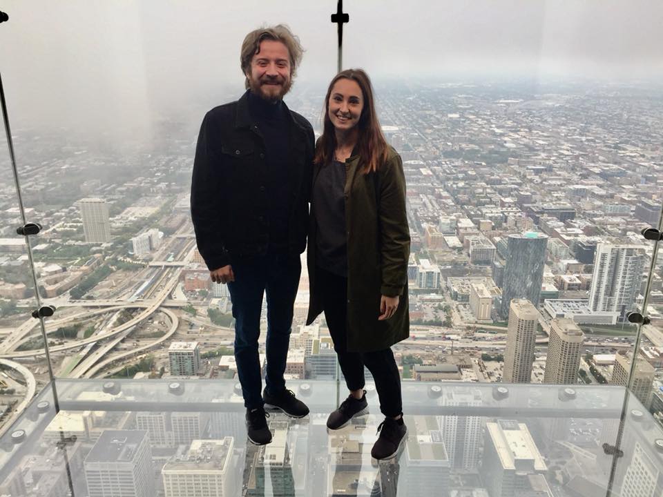 Couple standing in a glass box in a tower, Chicago city in the background