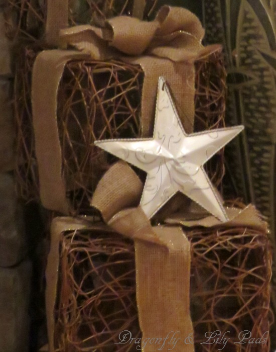 Packages made of twigs wrapped with burlap ribbon topped a metal white star nugged up to the fire place.