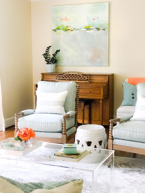 Light blue upholstery and a modern acrylic coffee table with a tray layered with decor - design by Sherry Hart. Come discover more inspiring trays for layering and vignettes in Adding Tray Tr&egrave;s Chic to Your Home.