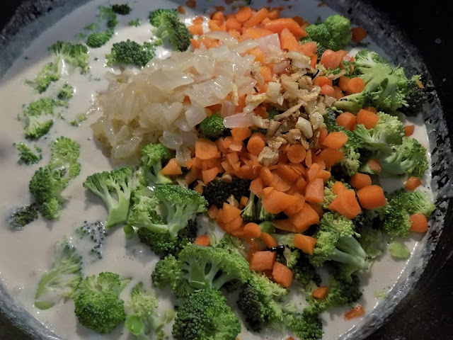 A picture of fresh broccoli and carrots topped with sauteed onions and garlic inside a large pot