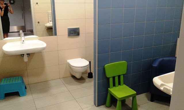 Pokój dla matki z dzieckiem Designer Outlet Gdańsk, w pokoju znajduje się fotel, krzesełko dla większego dziecka, przewijak, dwie toalety, umywalka.