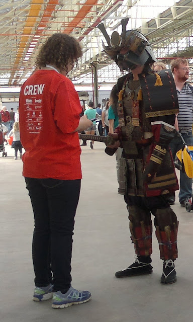 A Maker Faire crew member in red talks to a person dressed in traditional Japanese armour.