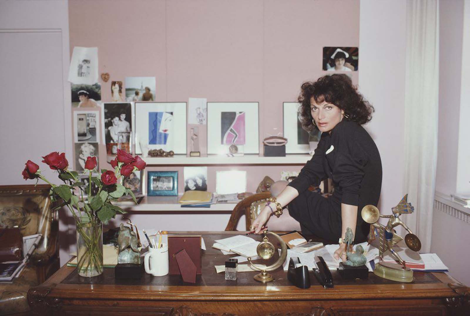 Belgian-born American fashion designer Diane Von Furstenberg in her studio. Furstenberg has very strong makeup, including gloss lipstick. She wears large hoop earrings and oversized bracelets and rings. She dresses in black, accented with a white pocket handkerchief on her chest. 1987.