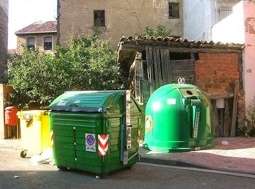 an closed green recycling dumpster surrounded by green garbage