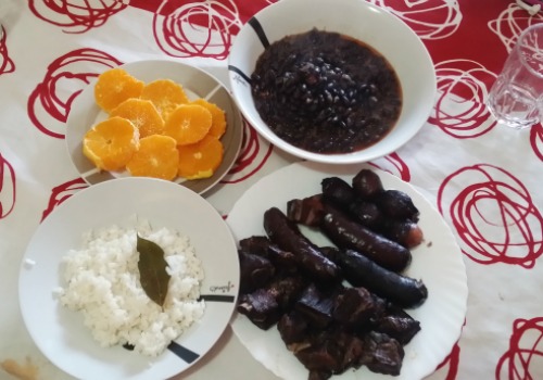 Platos por separado de carne y embutidos, naranja, arroz y frijoles